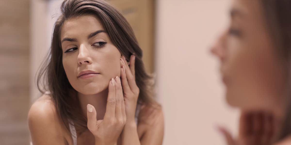 10 Really Weird Reasons You Have Bad Acne woman looking at herself from a mirror